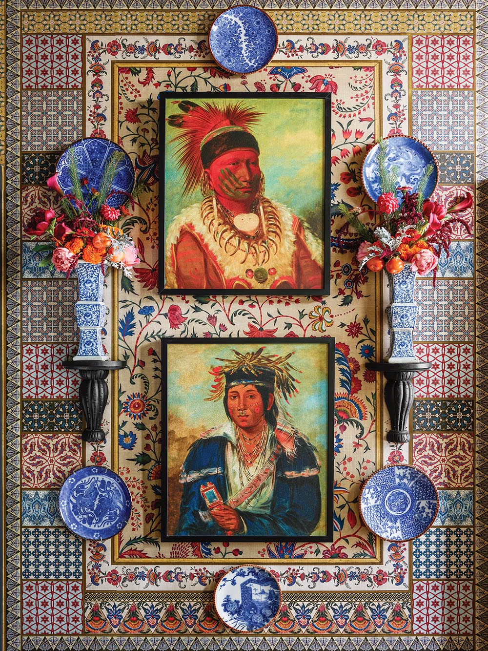 Wall of the entrance hall with Paul Montgomery wallpaper, paintings of native Americans, blue and white plates and vases of flowers.
