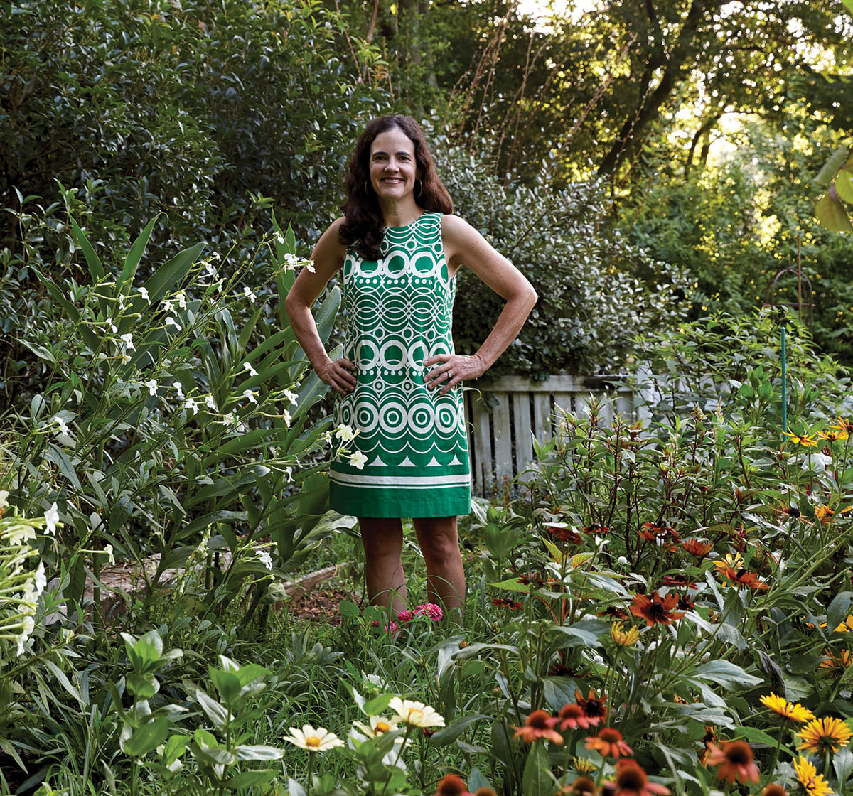 Floral designer Kappi Naftel stands in an abundant summer flower garden. She wears a green and white patterend sleeveless shift dress