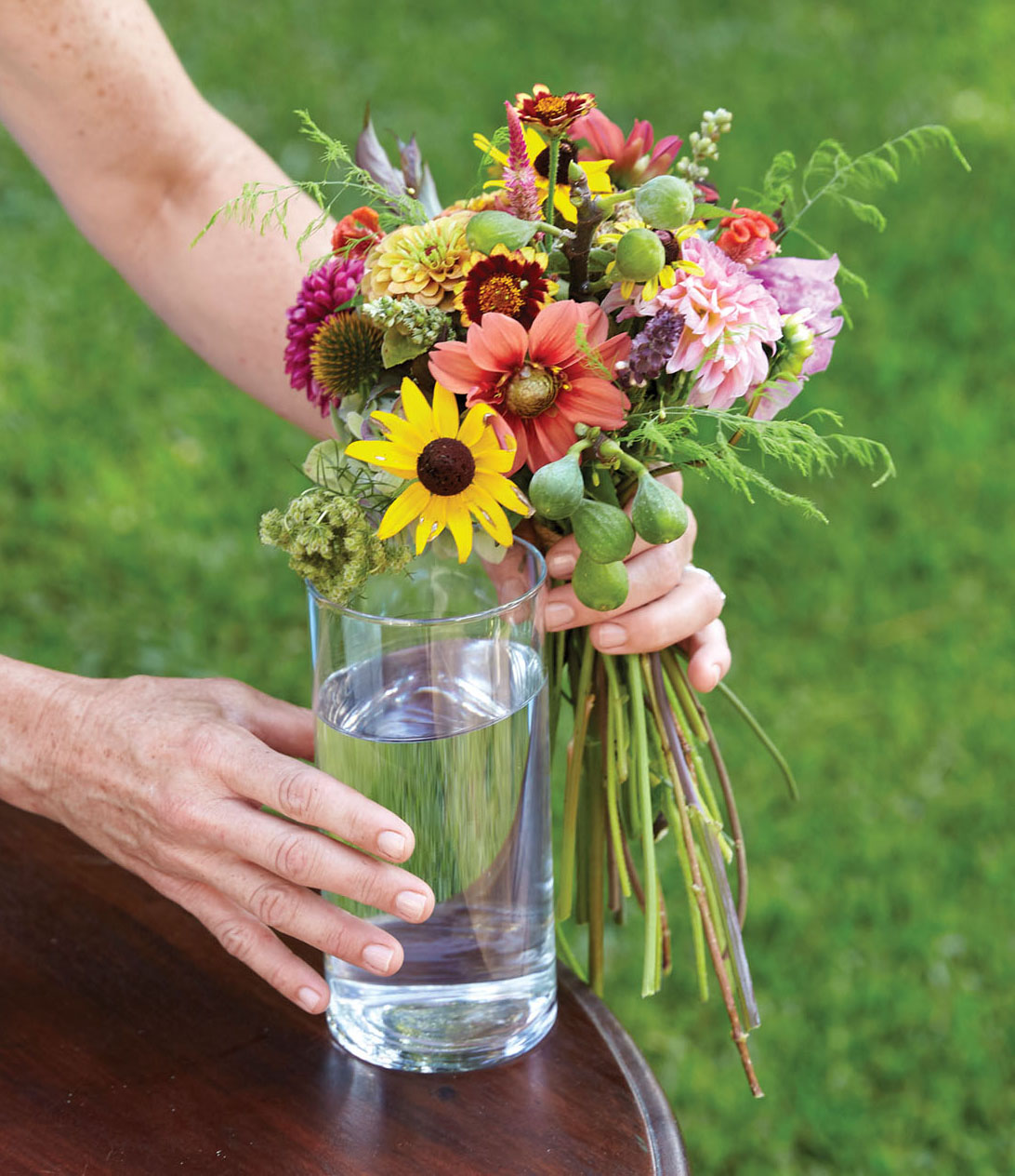 Kappi Naftel holds her bouquet against a glass to judge stem length. The bind point is near the top of the vessel.