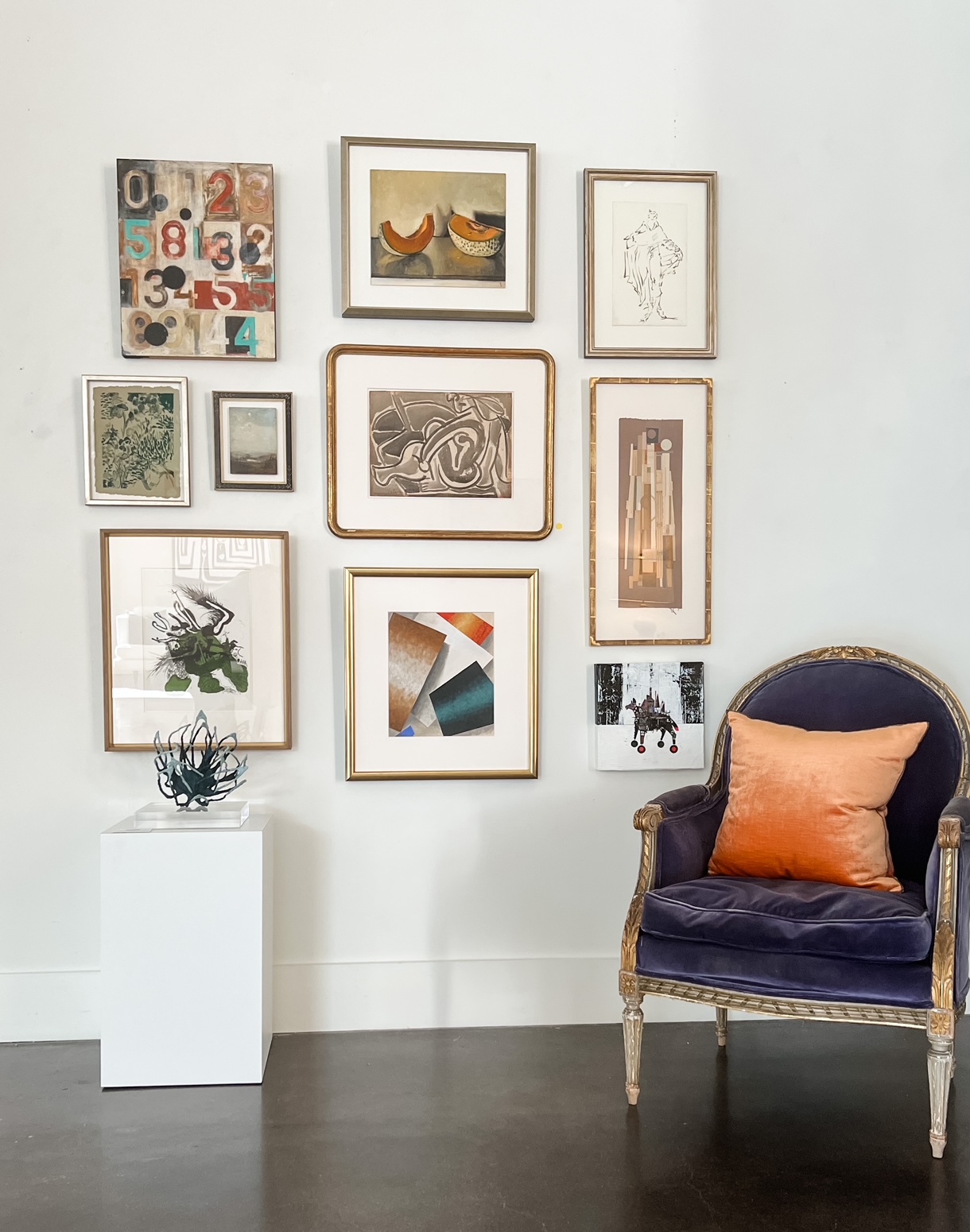 A gallery wall with gold frames behind a velvet chair.