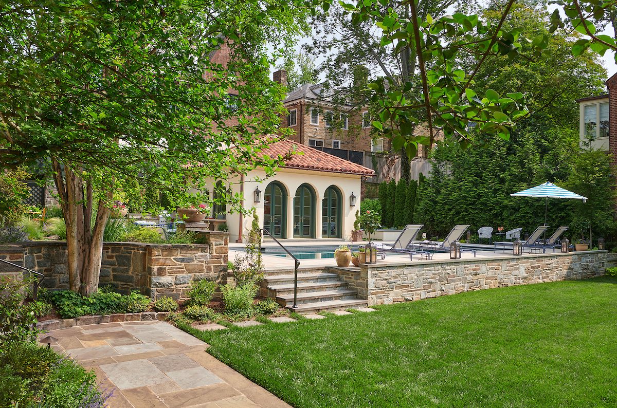 A fieldstone retaining wall gracefully sets off the pool courtyard. The landscape design provided for a sizable green lawn for the family dogs to run around which also makes an ideal croquet court.