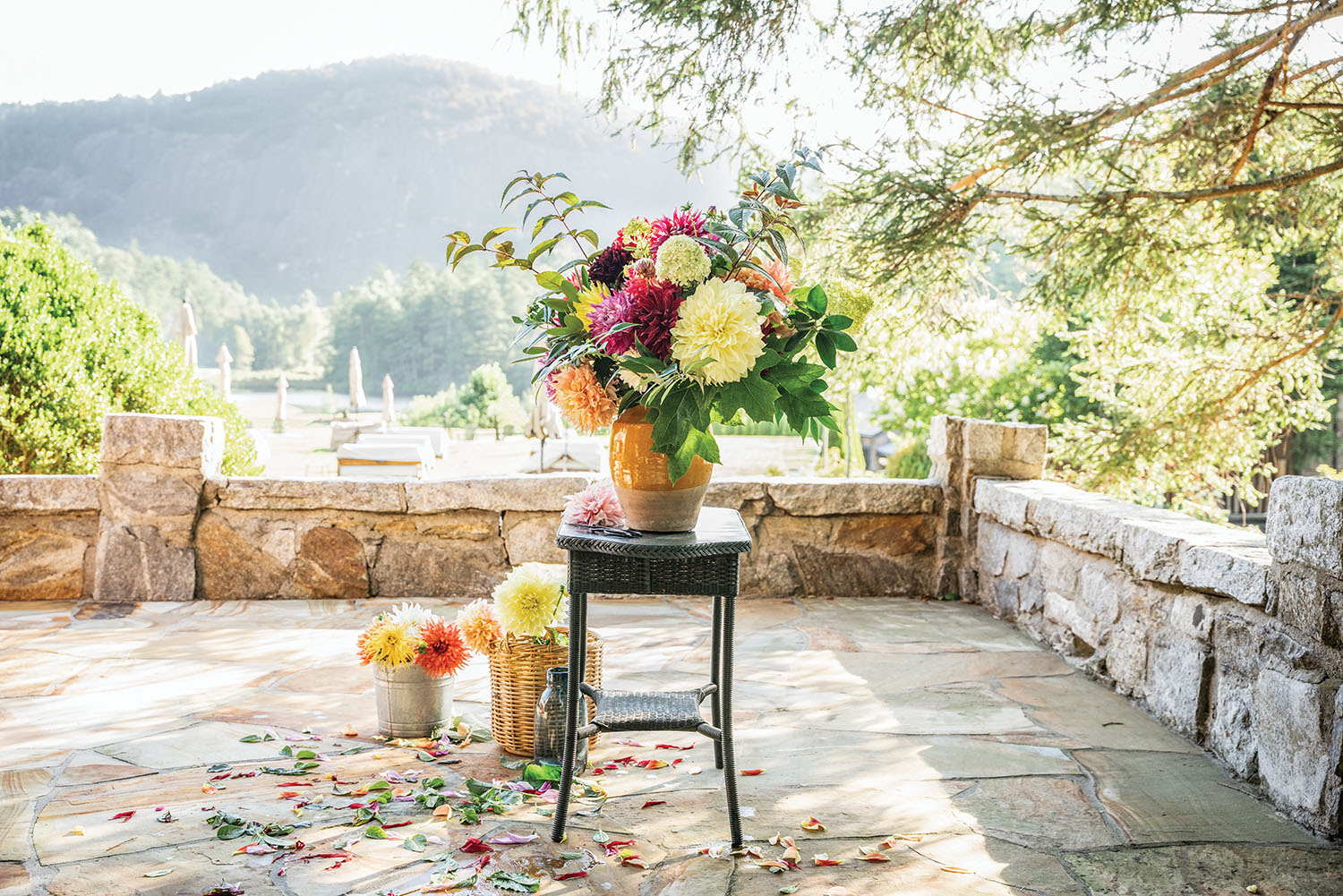 A vase full of fully colorful dahlias on a stool outdoors.