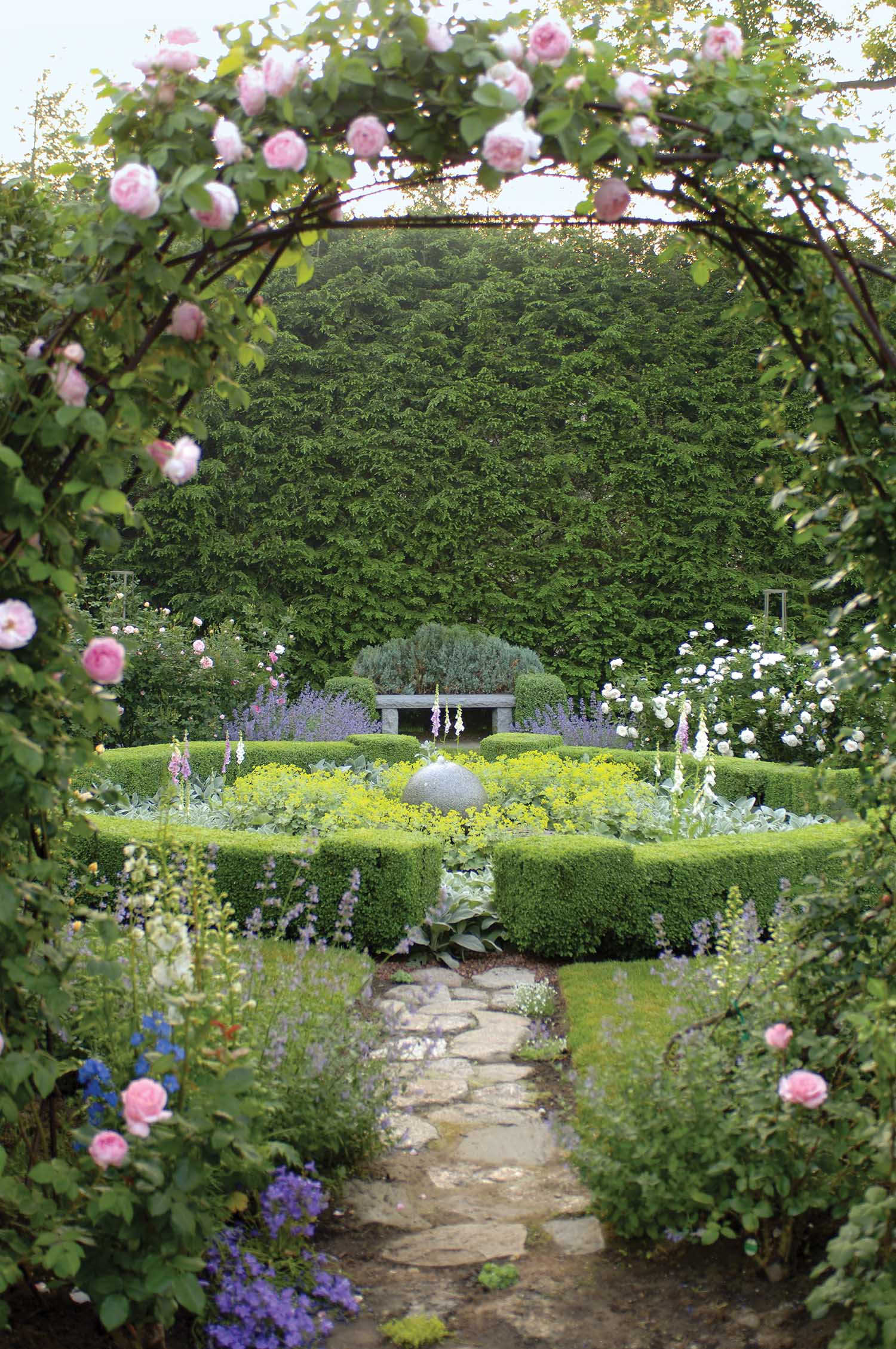 An arch of roses opens the entrance to a green garden.